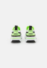 Baskets Puma au design blanc et noir, avec des accents verts, une semelle épaisse et une poignée à l'arrière pour un enfilage facile.