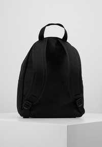 Czarny plecak z regulowanymi, wyściełanymi szelkami, gładkim materiałem, okrągłym kształtem i bocznymi kieszeniami; minimalistyczny design.