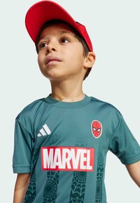 Maglietta atletica verde con logo di Spider-Man e testo "MARVEL". Presenta un motivo a ragnatela, maniche corte e tre strisce bianche su una spalla. Cappellino rosso.