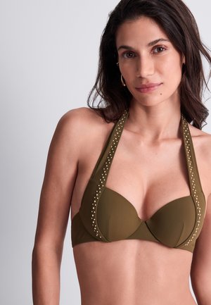 Femme aux longs cheveux foncés portant un haut de bikini olive clouté à col halter sur un fond clair uni.
