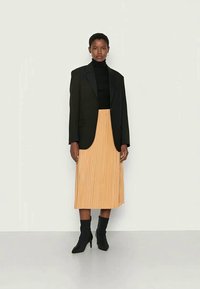 Black blazer over a black turtleneck, paired with a pleated, knee-length, light orange skirt and black ankle boots. Simple design and textures.