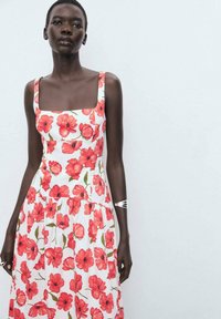 Floral dress with a square neckline, featuring red poppy flowers on a white background, flowing fabric, and a tiered skirt design.