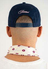 Căciulă de baseball albastră marină cu broderie roz "Interzis" pe spate; eșarfă crem cu modele geometrice în maro.