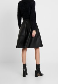 Svart läderkjol i midi-längd med en utsvängd design, som har en slät yta och en midja. Kombineras med svarta ankelboots.