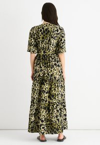 Maxi dress featuring short sleeves, a fitted waist, and tiered design. The fabric has a green and black leopard print pattern.