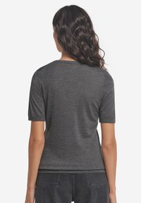 Grå kortærmet t-shirt med rund halsudskæring, glat tekstur og tætsiddende pasform. Sømdetaljer på skuldrene, kombineret med mørke denimbukser.
