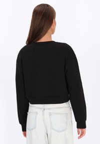 Fekete, rövidített szabású pulóver hosszú ujjakkal, puha anyagból készült, kerek nyakkivágással és laza hátsó résszel, világos farmerrel párosítva.