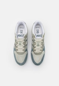 Beige and green athletic shoes with mesh and suede materials, featuring laces, a cushioned tongue, and "asics" branding on the tongue.