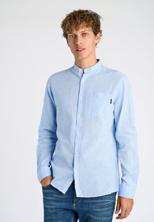 Camisa azul claro de botones con cuello de banda, mangas largas y un bolsillo en el pecho, hecha de tejido texturizado; combinada con jeans azules.
