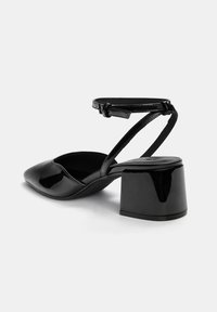 Crne lakirane slingback potpetice sa suženim prstom i blok petom. Traka oko gležnja ima podesivu kopču za sigurno prianjanje.