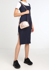 Granatowa, paskowana sukienka midi z bocznym rozcięciem, zestawiona z metaliczną torebką w kolorze różowego złota i czarnymi butami sportowymi.