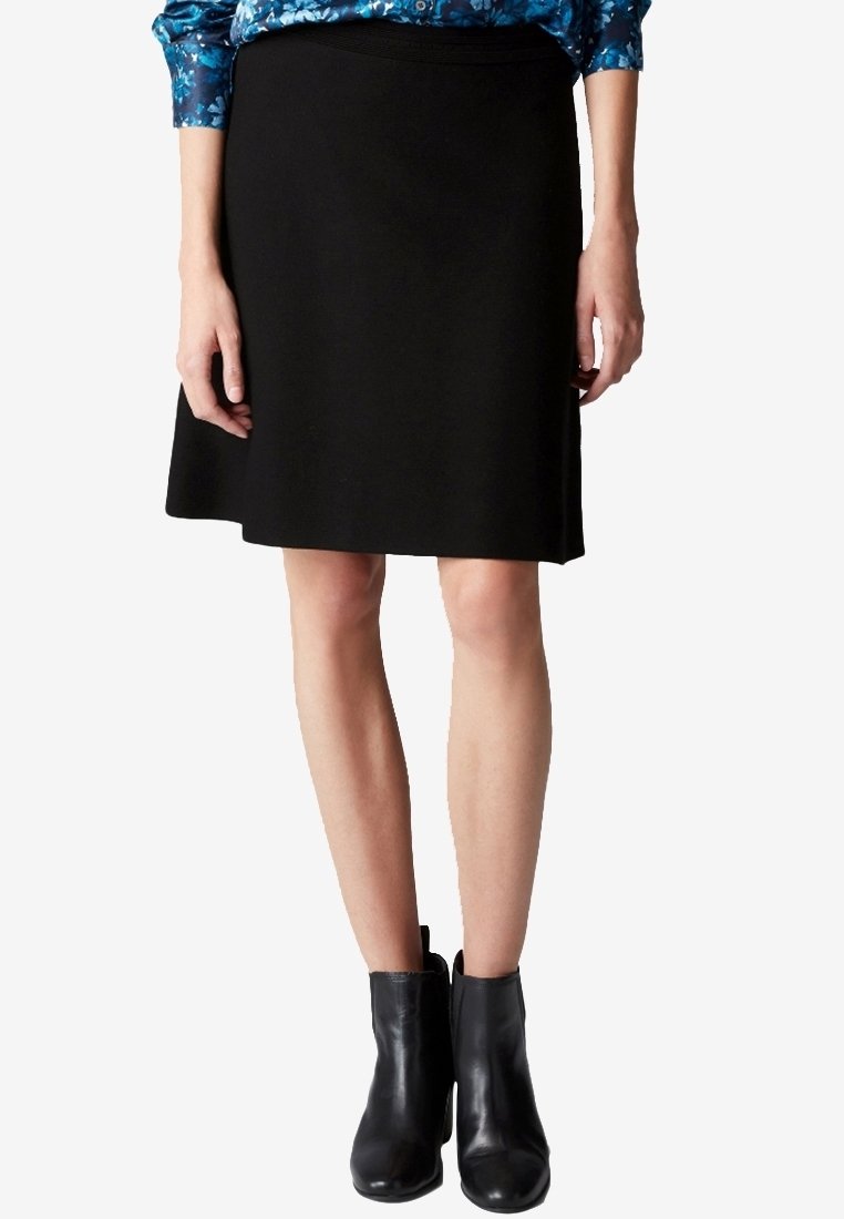 Gonna nera a trapezio realizzata in tessuto morbido, con cintura e taglio fino al ginocchio. Abbinata a stivaletti neri alla caviglia.