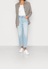 Rutig beige och brun skjortjacka, vit topp, ljusblå raka jeans, vita sneakers, avslappnad passform, mjukt tyg, synliga knappar.