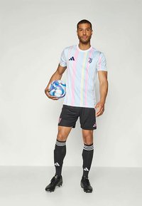 Juventus fotbaldrakt som har en pastelstripet kortermet skjorte, svarte shorts og svarte støvler. Holder en flerfarget fotball.