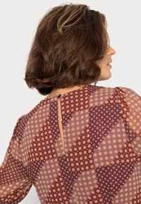 Blusa de padrão floral em tons de bordeaux com mangas bufantes, featuring pequenas flores amarelas e azuis, um fecho nas costas em forma de chave e tecido leve e macio.