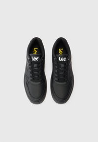 Mustad musta Lee spordijalatsite paar, millel on paelad, nähtav Lee logo keeltes, ja kollane logo sees. Kujutatud ülevalt valgel taustal.