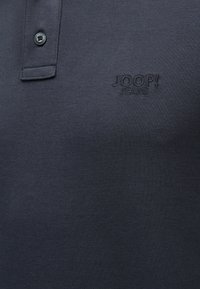 Σκούρο ναυτικό μπλε πλεκτό πόλο πουκάμισο με λοξή πλάκα δύο κουμπιών και κεντημένο λογότυπο "JOOP! JEANS" στο στήθος.