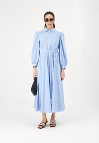 Απαλό μπλε φόρεμα μακρυμάνικο με φουσκωτά μανίκια, μαζεμένη μέση, λουλουδάτη κεντημένη διακόσμηση, συνδυασμένο με μαύρη τσάντα και πανέμορφα σανδάλια.