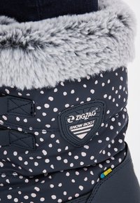Marineblaue Schneestiefel mit weißen Punkten, grauem Kunstfellkragen und schwarzem Zubehör, ausgestattet mit einem wasserdichten Etikett und Markenpatch.