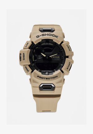 Orologio G-SHOCK tan con quadrante nero, presenta una cassa in resina, display digitale, grandi pulsanti, e contrassegnato con "PROTECTION" e "LIGHT."