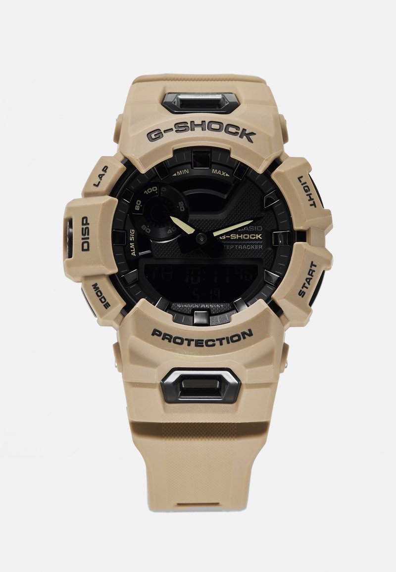 Montre G-SHOCK beige avec un cadran noir, dotée d'un boîtier en résine, d'un affichage numérique, de gros boutons, et marquée "PROTECTION" et "LIGHT".