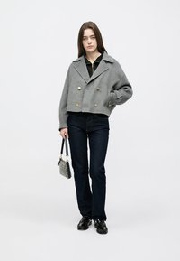 Sivá skrátená dvojradová bunda so zlatými gombíkmi, nosená cez čierny top, kombinovaná s tmavými džínsami a čiernymi topánkami, držiaca malú tašku.