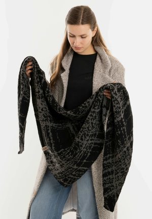 Châle noir et gris à motif, fait de tissu doux, présenté par une personne, drapant en forme triangulaire. Texture notable et design spacieux.