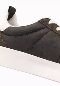 Brun syntetisk sneaker med vita skosnören och vit gummisula. Har en texturerad ovandel och kontrasterande sydda detaljer.