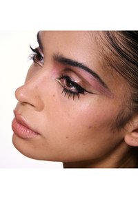 Primer plano de un rostro con sombra de ojos rosa y dorada, largas pestañas negras y una piel suave y radiante con sutiles pecas.