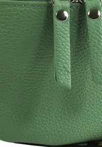 Groen, getextureerd leermateriaal met een rits aan de bovenkant met zilverkleurige accenten en decoratieve riemen aan de zijkant voor extra detail.