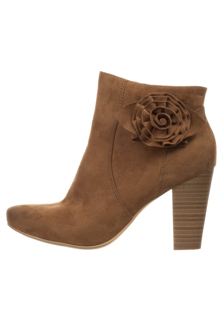 Bota de tobillo de ante marrón con una aplicación de rosa en el lateral, puntera afilada y un tacón rectángulo texturizado. Superficie suave con costuras visibles.