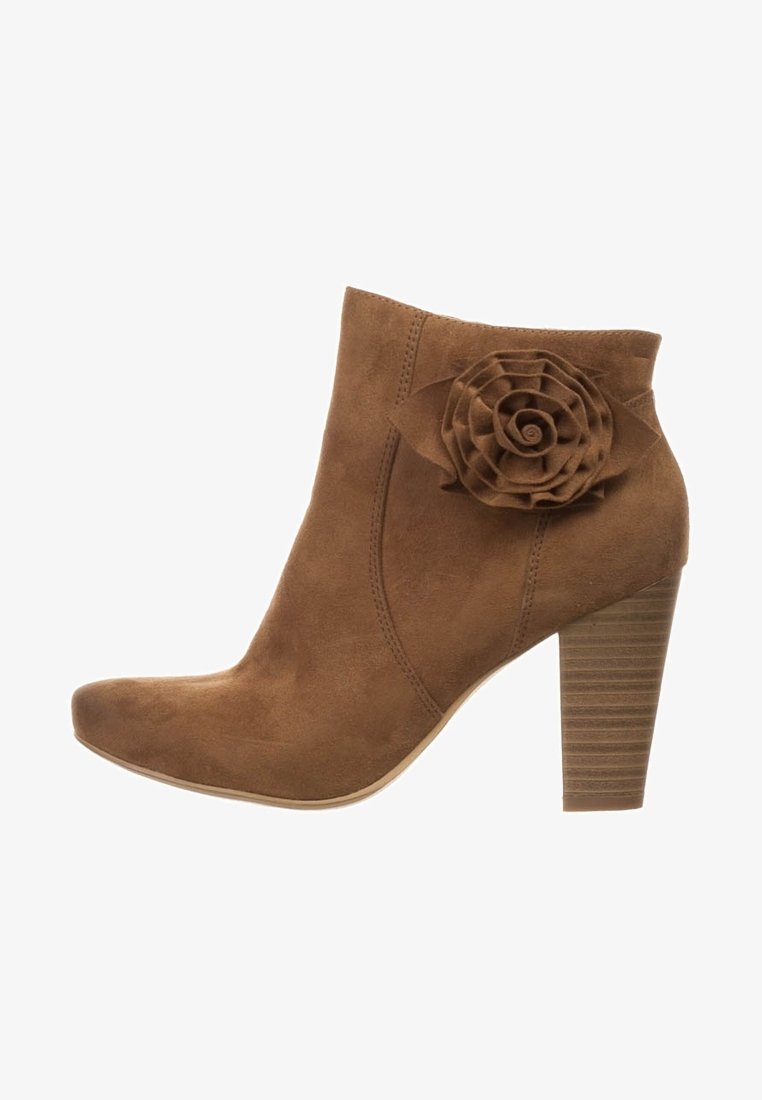 Bota de tobillo de ante marrón con una aplicación de rosa en el lateral, puntera afilada y un tacón rectángulo texturizado. Superficie suave con costuras visibles.