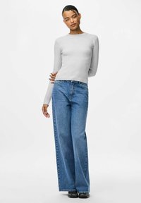 Pelēka ribota ilgs piedurkne tops, kas saskaņots ar platām ziliem džinsiem. Džinsiem ir klasiskā piecu kabatu dizains un izbalējis apdare.