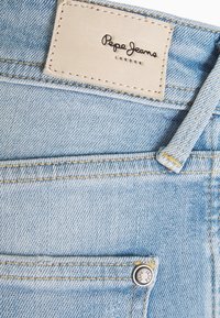 Ljusblå denimjeans med en läderlapp med "Pepe Jeans London" präglat. Synlig sömnad och en metallknappaccent.