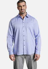 Hellblaues Langarmhemd mit einem feinen strukturierten Muster, schwarzen Knöpfen und einer Brusttasche; kombiniert mit grauen karierten Hosen.