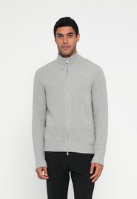 Camisola de malha cinzenta com fecho de correr, gola alta e mangas compridas, apresentando uma textura suave e detalhes subtis na bainha.