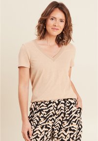 Beige V-hals t-shirt van zachte stof met korte mouwen, voorzien van verfijnde stiksel langs de halslijn. Gecombineerd met gestreepte zwart en crèmekleurige broek.