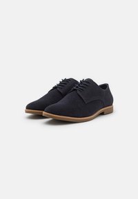 Chaussures habillées en suède bleu marine avec une finition lisse, bout arrondi et lacets fins. Semelle en caoutchouc marron avec un léger talon et des accents texturés sur le dessus.