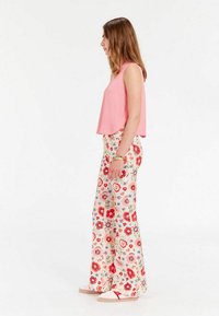 Haut sans manches rose associé à un pantalon large à fleurs avec des fleurs rouges et bleues sur fond beige. Le mannequin porte des chaussures claires.