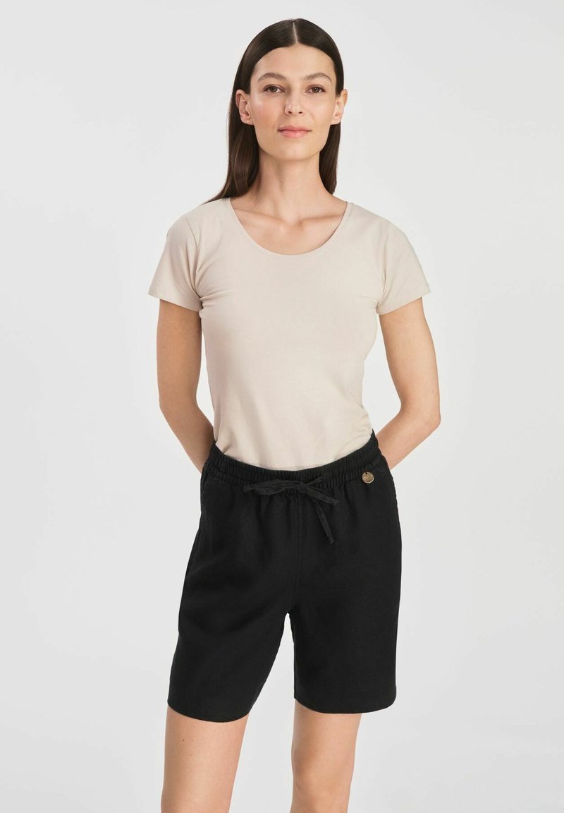 Beżowa bluzka z krótkim rękawem i okrągłym dekoltem, zestawiona z czarnymi, sięgającymi do kolan szortami z elastyczną talią i sznurkiem.