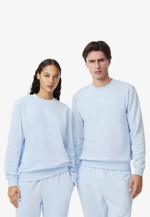Sweatshirts bleu clair en tissu doux, avec un col rond et des poignets côtelés ; inclut un petit logo blanc sur la poitrine.