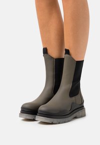 Botas de tobillo elásticas en verde oliva, con un diseño elegante, textura suave, material duradero y una suela gruesa transparente.