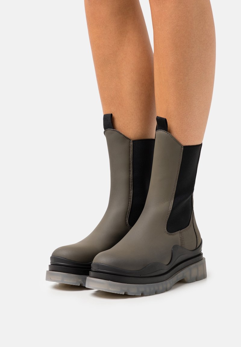 Botas de tobillo elásticas en verde oliva, con un diseño elegante, textura suave, material duradero y una suela gruesa transparente.