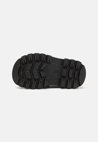 Suela de zapato de goma con patrones de profundidad, que presenta amplias ranuras y una superficie texturizada para un mejor agarre. Color negro predominante en toda su extensión.