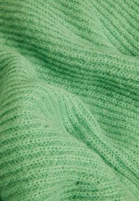 Tissu tricoté vert clair, doux, avec une texture côtelée, présentant des plis et une apparence duveteuse et confortable.