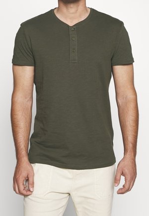 Oliwkowa, krótka koszulka henley z trzema guzikami przy dekolcie, wykonana z miękkiej tkaniny, o prostej, dopasowanej sylwetce.