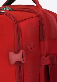 Červený batoh na zip s odolnou tkaninou, texturovaným povrchem, bočním zavíráním a charakteristickým detailem ve tvaru kruhu.