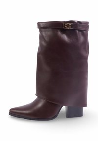 Botte en cuir marron avec un haut relâché, bout pointu et talon bloc. Présente une sangle décorative avec une boucle dorée au niveau du revers.