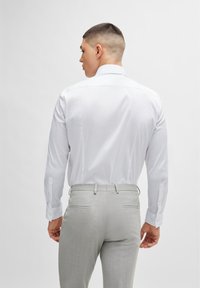White long-sleeve shirt with a smooth texture and buttoned cuffs, paired with light grey textured trousers featuring back pockets.