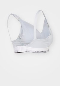 Gaiši zils bezvadu krūšturis ar regulējamiem siksniņām, gluda auduma virsma un balta josla ar melnu "Calvin Klein" zīmola apzīmējumu apakšā.